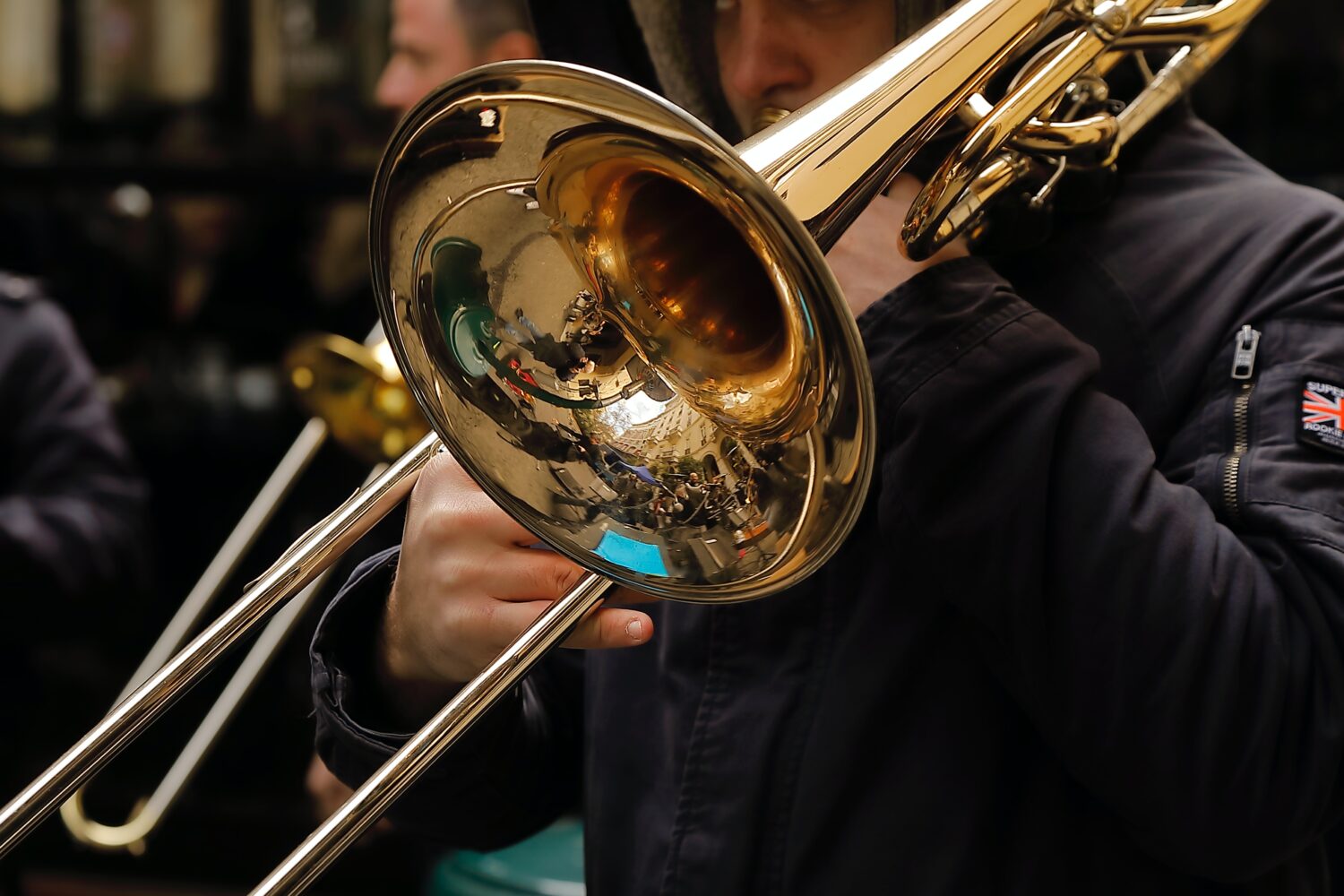 Bild på en blank mässingfärgad trombon som någon spelar. I den blanka tratten speglas lokalen.